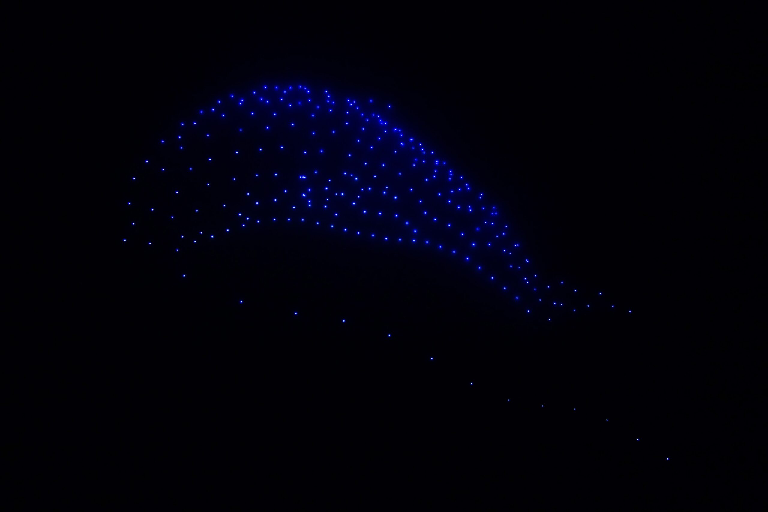 Blue lights from synchronized drones during a drone show forming abstract patterns in the night sky.
