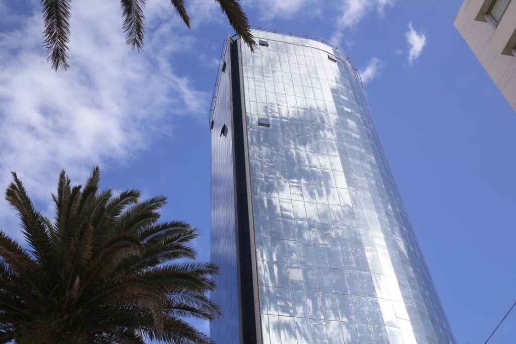 Glass tower of the World Trade Center building in Punta del Este, reflecting the sky and surrounded by palm trees.